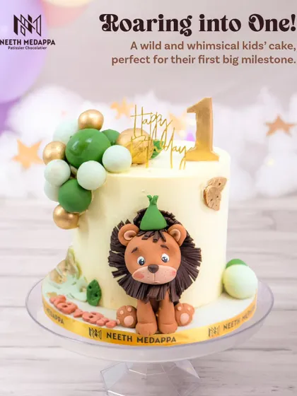 Roaring into one! This adorable first birthday cake features a cute lion king wearing a party hat, surrounded by a balloon-like arrangement of green and gold spheres.