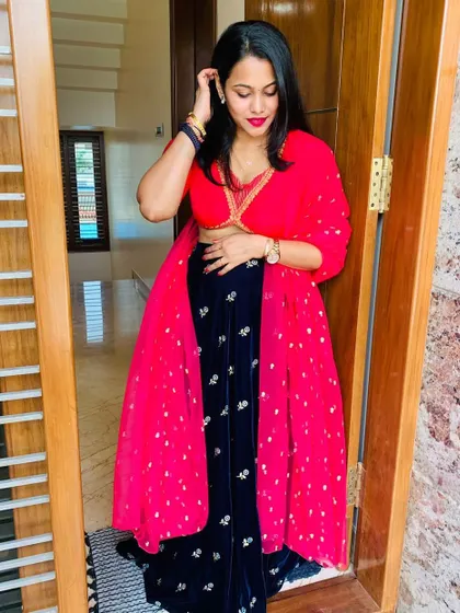 A stylish pose from a happy client in her custom outfit. The combination of the red crop top, embroidered velvet skirt, and sheer dupatta creates a modern and festive look.