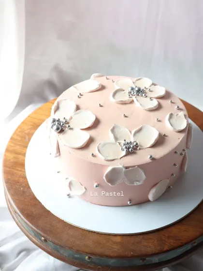 The full view of the pink cake with white floral details, sitting on a rustic wooden cake stand.