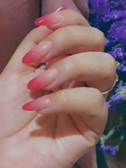 A classic red ombre effect on sharp, almond-shaped nail extensions, blending from a sheer nude base to a vibrant red tip for a seamless gradient look.