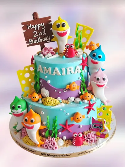 A vibrant two-tier Baby Shark cake for a second birthday. The cake is decorated with the entire shark family and other sea creatures, creating a fun underwater scene.