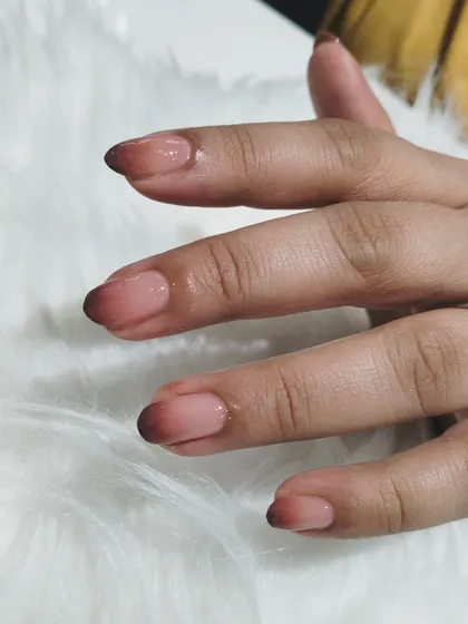 A moody and sophisticated ombré on short, natural nails, blending from a sheer nude base to a deep brown, almost black, tip.