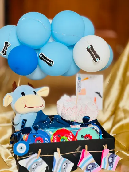 A bright, clear shot of the baby boy hamper without the lights. The blue theme is consistent throughout, from the toys and bibs to the decorative balloons.