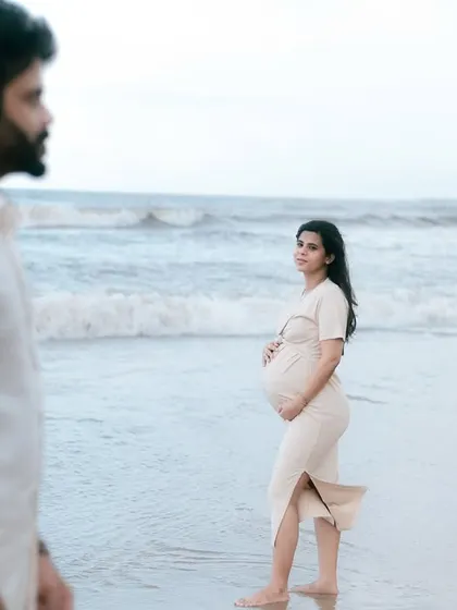 This shot captures the mother-to-be looking back towards her partner, her hand resting on her bump. It tells a story of partnership and the shared journey of pregnancy against the beautiful ocean backdrop.