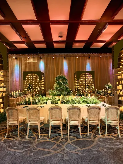 A long dining table set for an intimate feast, surrounded by candle walls and featuring a lush floral runner, creating a warm, glowing, and opulent atmosphere.