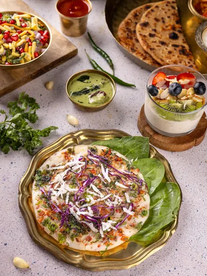 A traditional Indian breakfast platter with uttapam, paratha, and fruit yogurt, showcasing a wholesome and diverse meal.