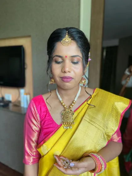 A beautiful South Indian bride in a vibrant yellow and pink silk saree. The makeup features defined eyes and a bold pink lip to match her blouse.