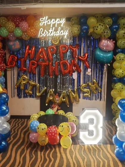 A bright and colorful birthday setup packed with fun elements. This design combines a 'Happy Birthday' neon sign, red foil balloons for the name, a marquee number '3', and columns made of multi-colored and smiley-face balloons.