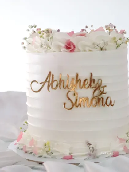 A simple and beautiful cake for a couple's special day. The clean, textured frosting is decorated with fresh flowers and a custom gold name topper.