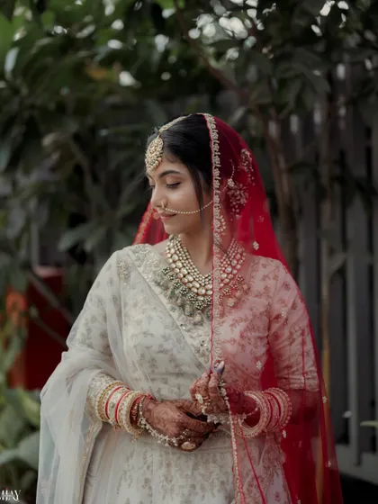 A classic portrait of the bride in her white lehenga and red veil, looking down with a gentle smile.