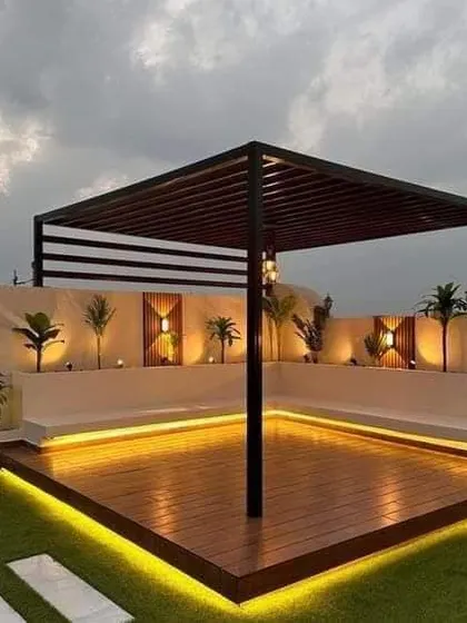 A stunning rooftop lounge with a wooden deck, built-in seating, and a pergola. The under-seat LED lighting creates a beautiful ambiance against the evening sky.