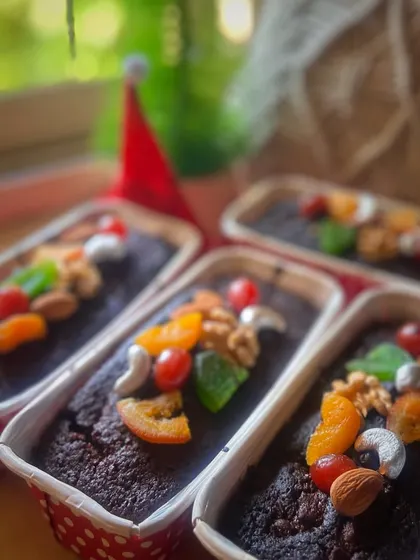 Our Christmas plum cakes come in small tins, with fruit-and-nut decorations across the tops and seasonal styling around them.