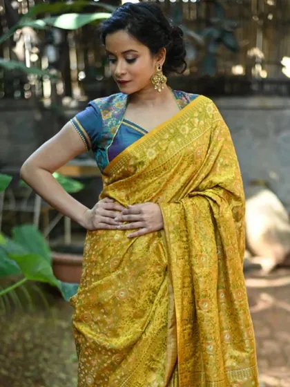 A model in a yellow printed saree wears a cap-sleeve blouse and accessorizes with large traditional earrings.