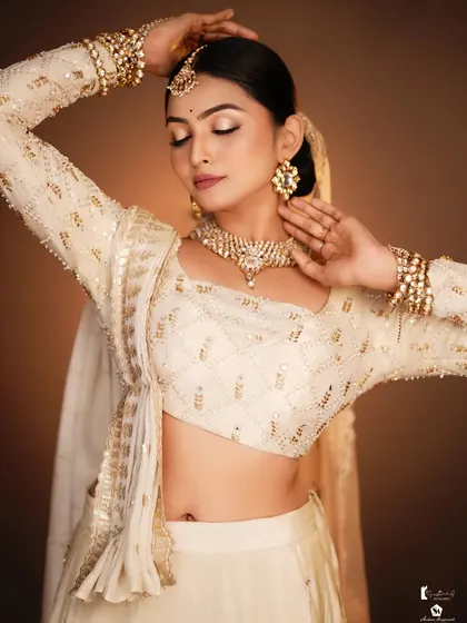 The soft, warm lighting enhances the golden tones in the outfit and makeup.