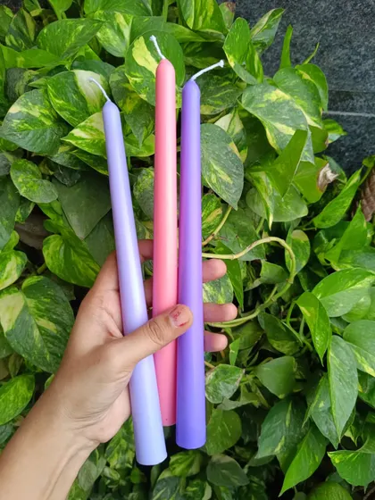 A trio of taper candles in pastel shades of lavender, pink, and purple.