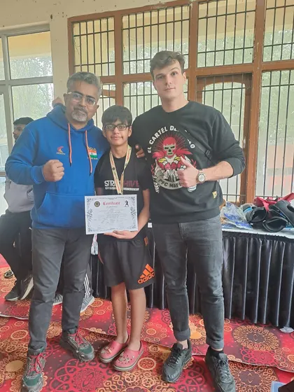 A young competitor receives his medal and certificate, flanked by his proud coaches.