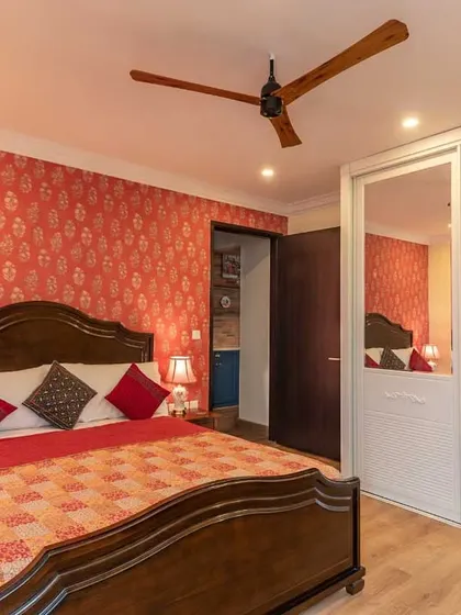 A cozy guest bedroom featuring a vibrant red patterned wallpaper and a classic wooden bed. The mirrored wardrobe doors help to make the room feel more spacious.
