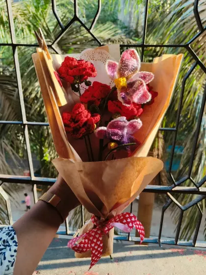 A beautiful combination of deep red roses and delicate crochet orchids. This bouquet has a rustic feel with the brown paper wrapping and heart-patterned ribbon.