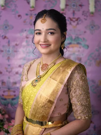 A bride looking lovely in a lime green and pink Kanchipuram saree. Her custom pink blouse features delicate gold embroidery on sheer sleeves for a modern touch.