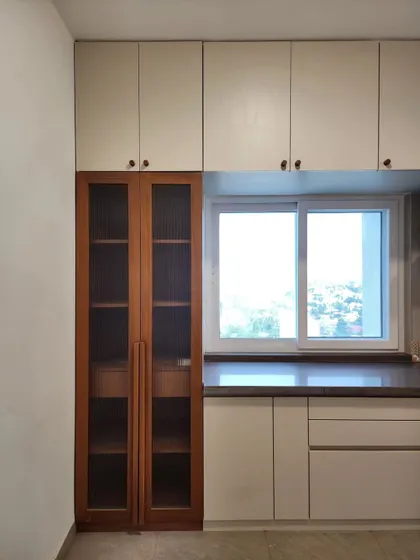 A kitchen storage unit designed to maximize space and light. The tall, glass-fronted cabinet provides elegant display storage, while the large window brings in ample daylight, making the kitchen feel bright and airy.