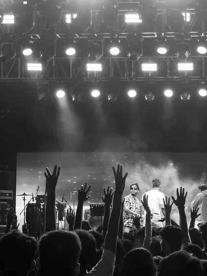 A black and white perspective from the back of the venue, focusing on the audience's participation with hands raised in the air, creating a powerful, timeless concert image.