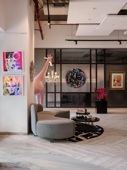 We create distinct zones within our gallery to evoke different moods. This corner features a whimsical giraffe sculpture holding a chandelier alongside neon artworks, demonstrating how we blend functional design with surreal pop art.