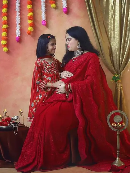 The special bond between a mother and her daughter as they wait for the new baby. The flowing red saree and traditional decor make this maternity photo feel so timeless and elegant.