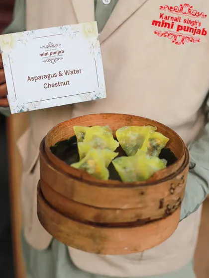 Our Asparagus and Water Chestnut Dimsum, presented by a server in our signature uniform. These vegetarian dumplings are a perfect example of our commitment to gourmet global cuisine.