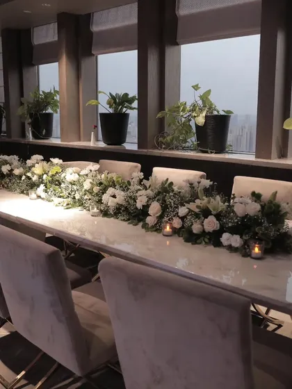 A long marble-top table set for an executive dinner. The simple yet elegant floral runner and candlelight create a sophisticated ambiance, perfect for high-level corporate meetings or client dinners.