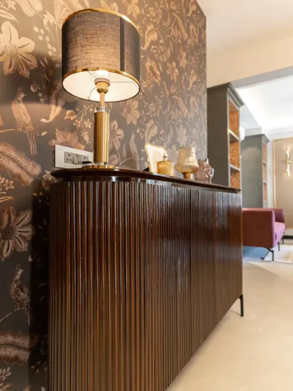 A detailed shot of the fluted console and the elegant table lamp. The rich textures of the wallpaper, the wood, and the lampshade come together to create a sophisticated and tactile experience.