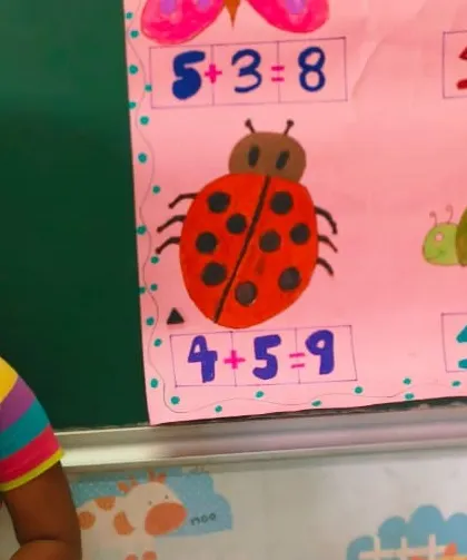 A student uses a colorful chart with ladybugs and turtles to make learning addition a fun and visual experience for her peers.
