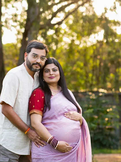 A classic couple's portrait taken outdoors with soft, flattering light. The mom-to-be is glowing in a lavender saree.
