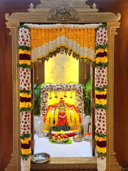 A stunning Varamahalakshmi decoration for a pooja room, with intricate flower columns and a beautiful backdrop for the goddess.