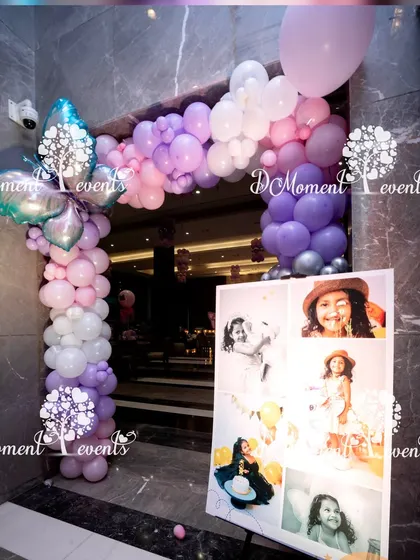 A simple and elegant photo collage board for a third birthday, framed by a beautiful arch of lavender and pink balloons.