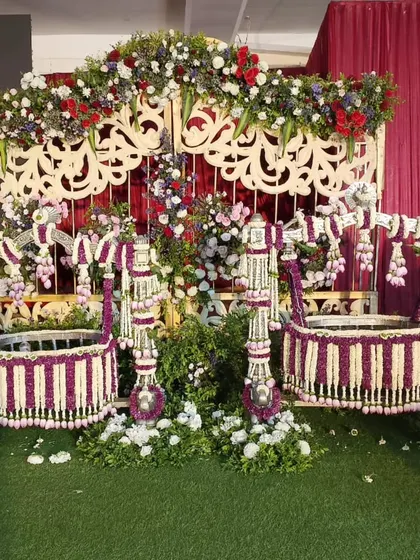 A unique cradle decoration featuring two cradles for a twin naming ceremony, both adorned with purple and white flowers.