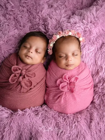 A beautiful portrait of twin babies nestled together on a soft purple rug. Coordinating wraps with different floral knot styles adds individuality while maintaining a cohesive look.