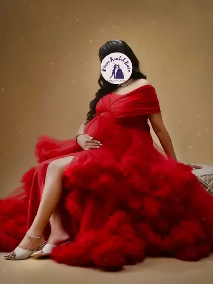 A seated portrait in the studio featuring the vibrant red ruffled gown. This pose allows the dress's voluminous skirt to spread out, creating a truly glamorous effect.