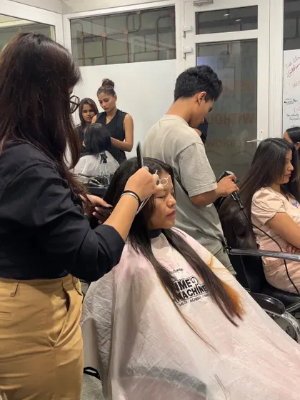 A student practices a haircut on a live model, with a trainer providing guidance and support.