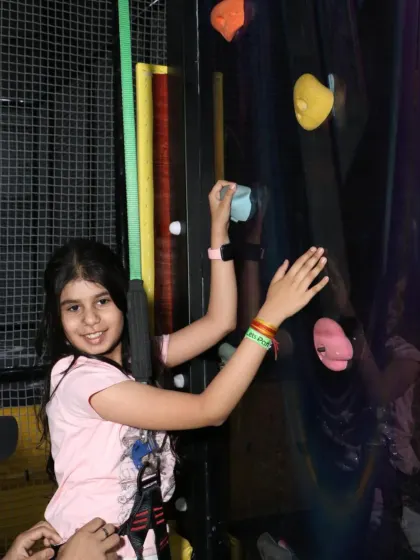 A girl carefully plans her next move on the climbing wall, a great activity for focus and physical fitness.