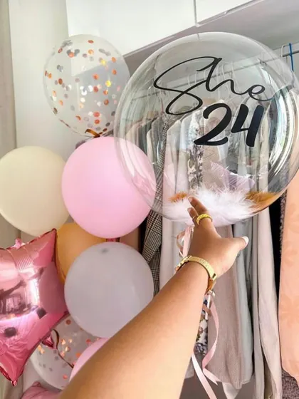 A fun and flirty bunch for a 24th birthday. This arrangement includes a personalized "She's 24" bubble balloon filled with feathers, along with a mix of pastel and foil balloons.