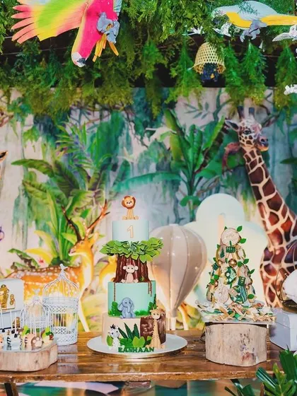 A magical cake table setup for Eshaan's jungle party. The table is surrounded by dense greenery, animal figures, and a custom jungle-themed cake, all under a canopy of hanging decorations.