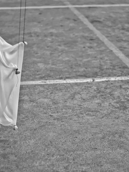 A single, simple marionette made of white cloth stands on the ground. This artistic, black and white shot highlights the elegant simplicity of handmade puppets.