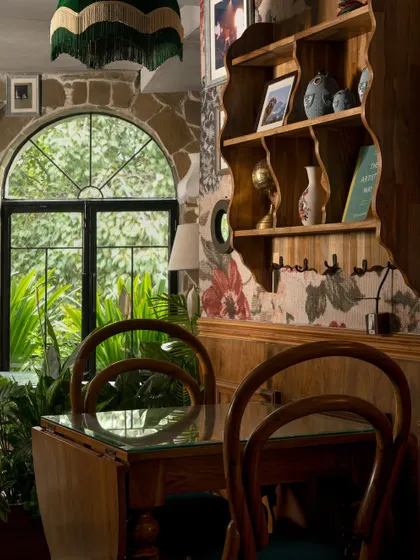 Another view of the intimate seating at Echoes. The mix of bentwood chairs, a glass-topped table, and floral wallpaper against a stone arch creates a layered, maximalist aesthetic that feels both personal and curated.