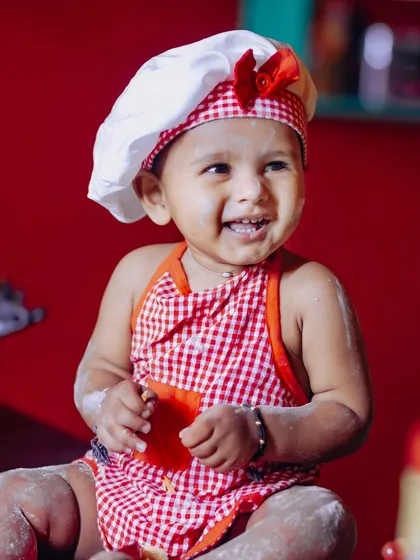 Dressed as a little chef, this baby girl is all smiles and covered in flour, ready to "bake" her own cake.