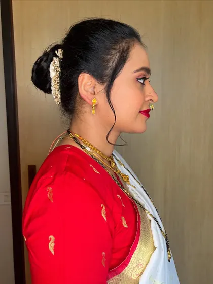 A side profile showing the elegant hair updo for this Nauvari saree look. The neat bun is accented with a gold accessory and soft tendrils to frame the face.