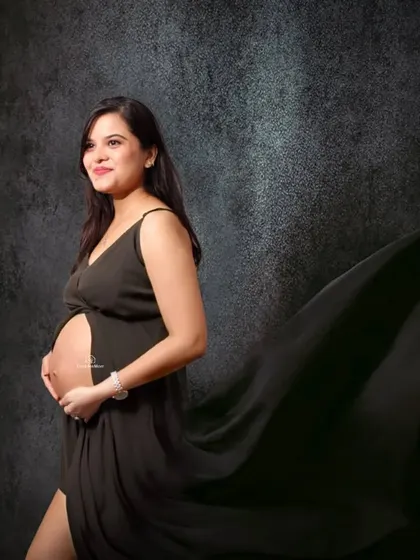 Classic elegance in a black gown with a flowing train. This studio portrait uses a dark, textured background to create a moody and sophisticated look that emphasizes the pregnancy silhouette.