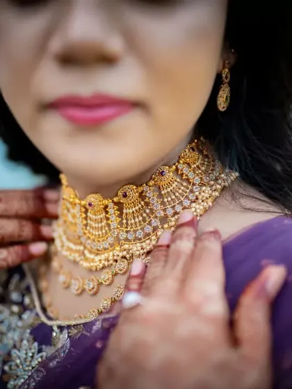 A detailed shot focusing on a bride's exquisite gold choker necklace and the intricate henna design on her hands.