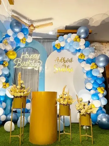 A bright and cheerful birthday decoration in a home setting. This setup uses a blue, white, and gold color palette with dual arched backdrops, a neon sign, and floral accents.