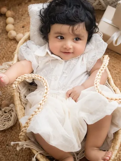 An adorable portrait of the six-month-old baby girl in her white dress, surrounded by soft, neutral props.