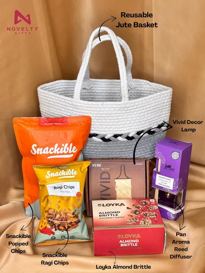 This hamper combines indulgence with utility. It features a reusable jute basket filled with snacks from Snackible, Loyka almond brittle, a vivid decor lamp, and a pan-aroma reed diffuser.